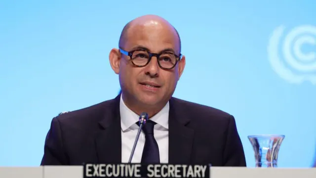 Simon Stiell seated at a microphone with an Executive Secretary nameplate