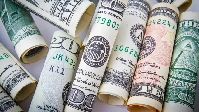 An assortment of rolled U.S. currency notes in various denominations, including one, five, ten, and twenty dollar bills, arranged side by side