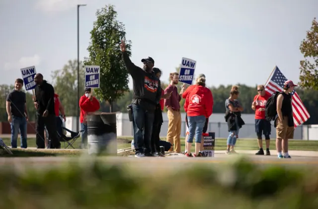 A line of UAW picketers holding signs and U.S. flags