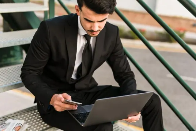 A man using a phone beside an open laptop