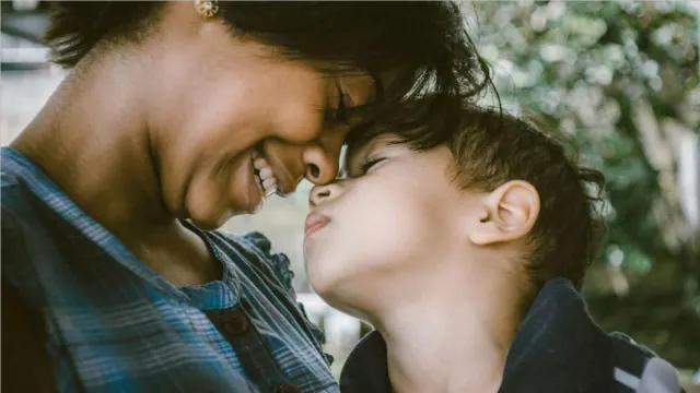 A close-up view of a woman embracing her child with green trees in the background.