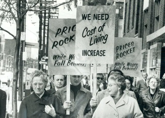 A black-and-white photograph of demonstrators carrying cost-of-living signs