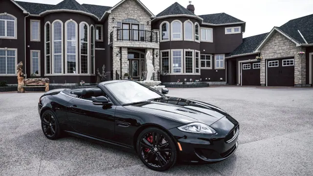 A dark convertible parked in front of a large house