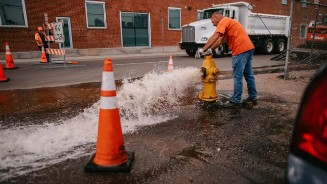 A worker operating a fire hydrant beside a street