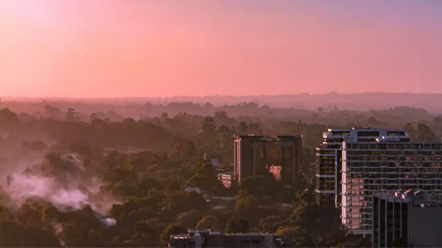 A city skyline at sunset with a plume visible in the distance