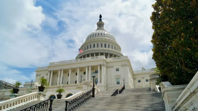 Stairs leading up to the U.S. Capitol building, seen underneath a cloudy blue sky.