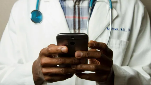 A doctor wearing a white lab coat and a stethoscope using their phone.