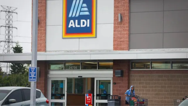An Aldi storefront is pictured, along with a customer who is taking groceries to her cart.
