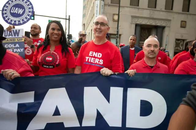 People in red shirts behind a UAW rally banner
