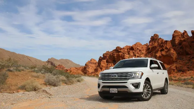 A white car left on the side of the road. The car appears to be in the middle of nowhere and is surrounded by sand and rocks