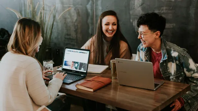 Three people talking around a table with laptops