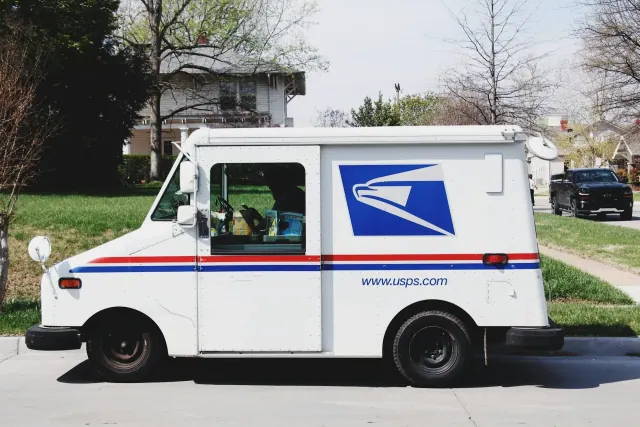 A white mail van bearing the logo of USPS parked in front of lawn