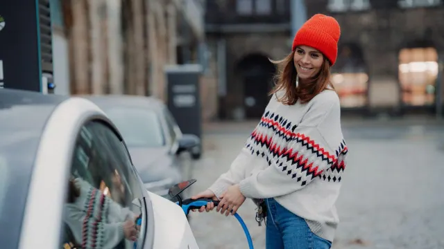A person standing beside a car and charging connector