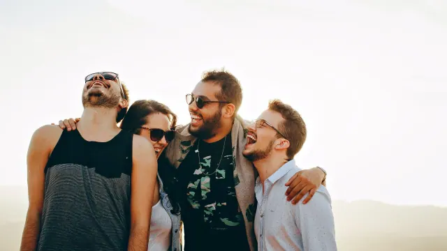 Four people laughing with their arms around one another