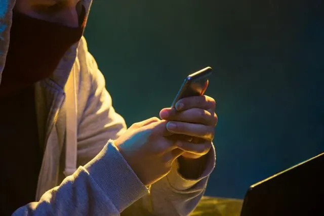 Illustrative photograph of a person using a smartphone beside a laptop