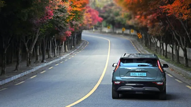 A vehicle traveling along a road bordered by autumn trees