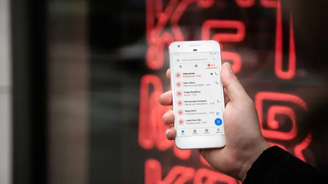 A person holding a white smartphone. The screen is on and shows a list of messages and missed phone calls.