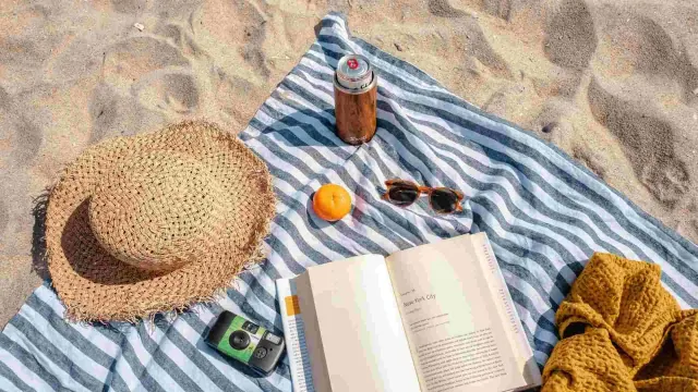 A beach blanket with a hat, drink, sunglasses, camera and open book