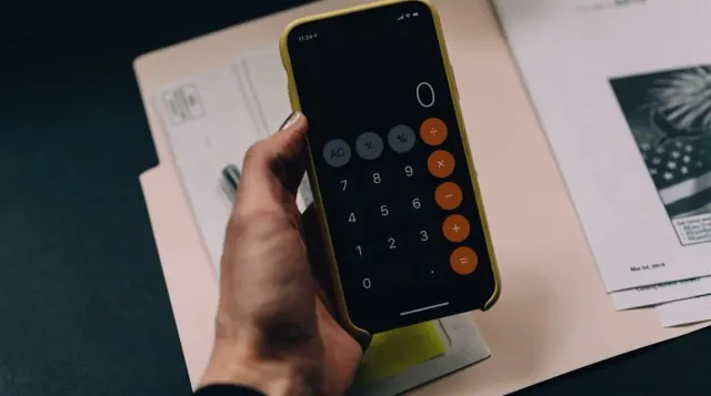 A person using a phone calculator beside bills
