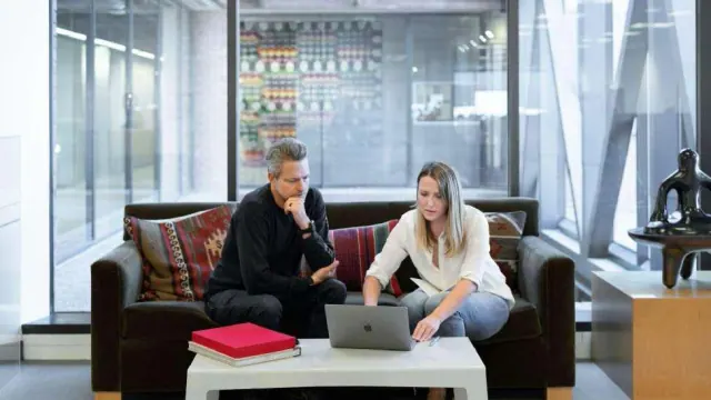 Two people looking at a laptop while seated on a sofa