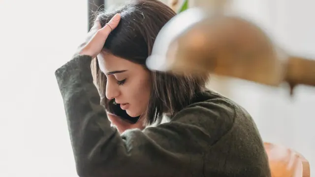 A woman on a phone call. She is holding the phone to her ear and running her hand through her hair. She looks worried.