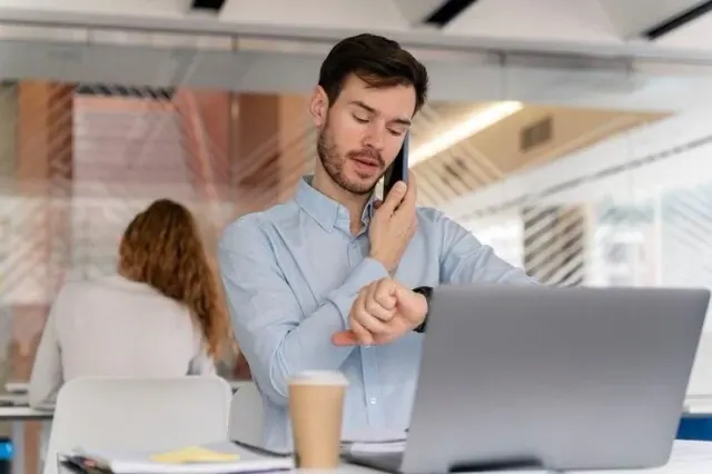 A person looking at a watch beside a laptop