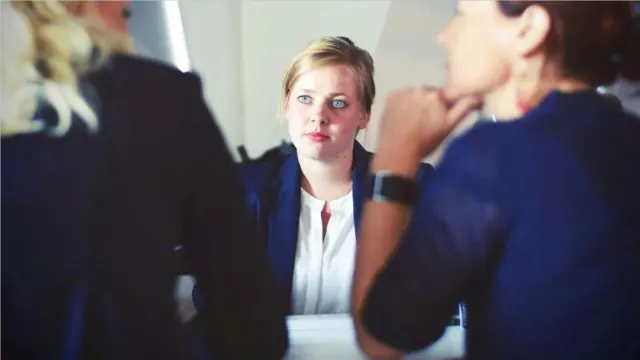 A woman sits before two other women at a table in an office.