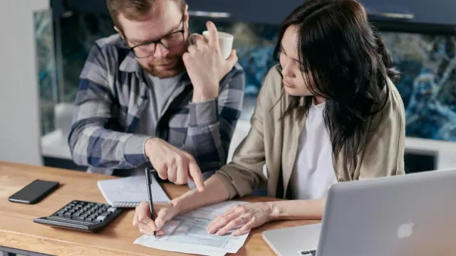 Two people reviewing bills beside a laptop