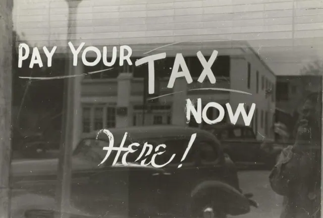 A black and white picture of a message on the window saying Pay Your Tax Now Here!
