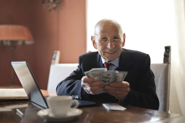 A man in a suit holds several US dollar bills in his hands while smiling