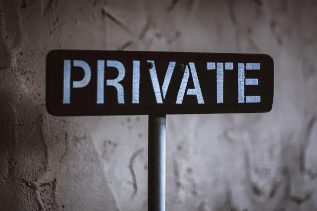 A black and white sign saying Private against a concrete wall background