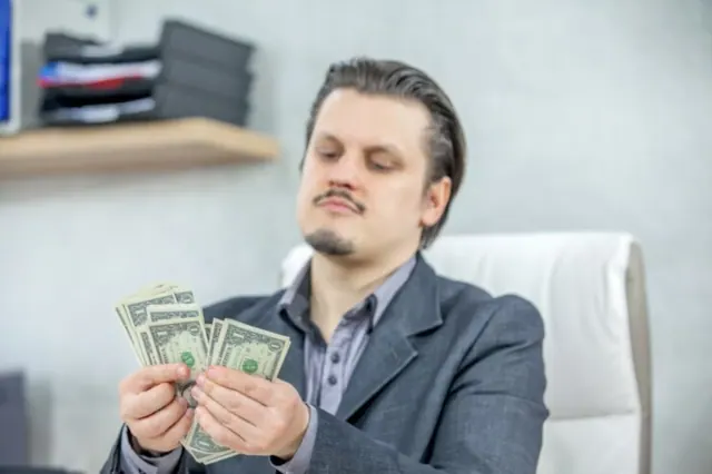 A man dressed in a grey suit is pictured counting several dollar bills