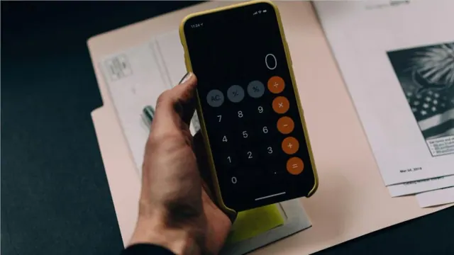A person holds their phone open to the calculator app in front of files and folders.
