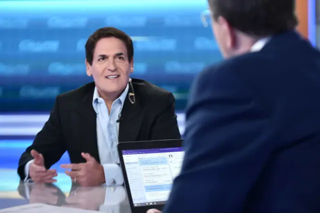 Mark Cuban speaking with an interviewer at a table