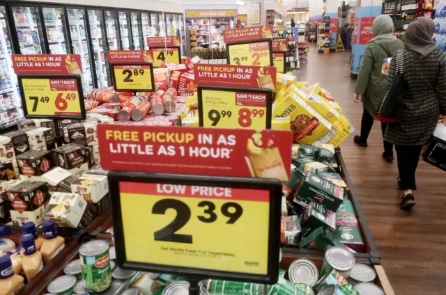 Shoppers beside grocery displays with price signs