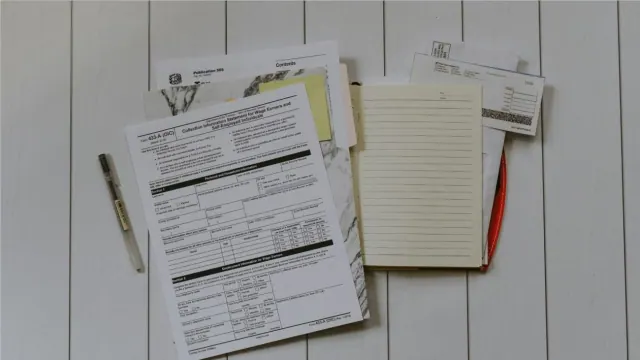 A stack of financial papers beside a pen on a white surface.