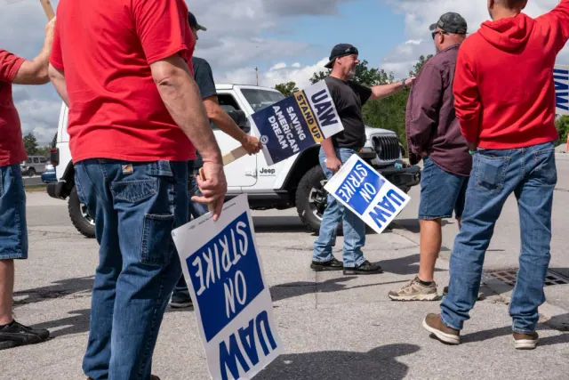 People holding UAW On Strike signs beside a roadway